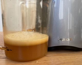 Hurom H-AA slow juicer with yield of apple juice in plastic jug