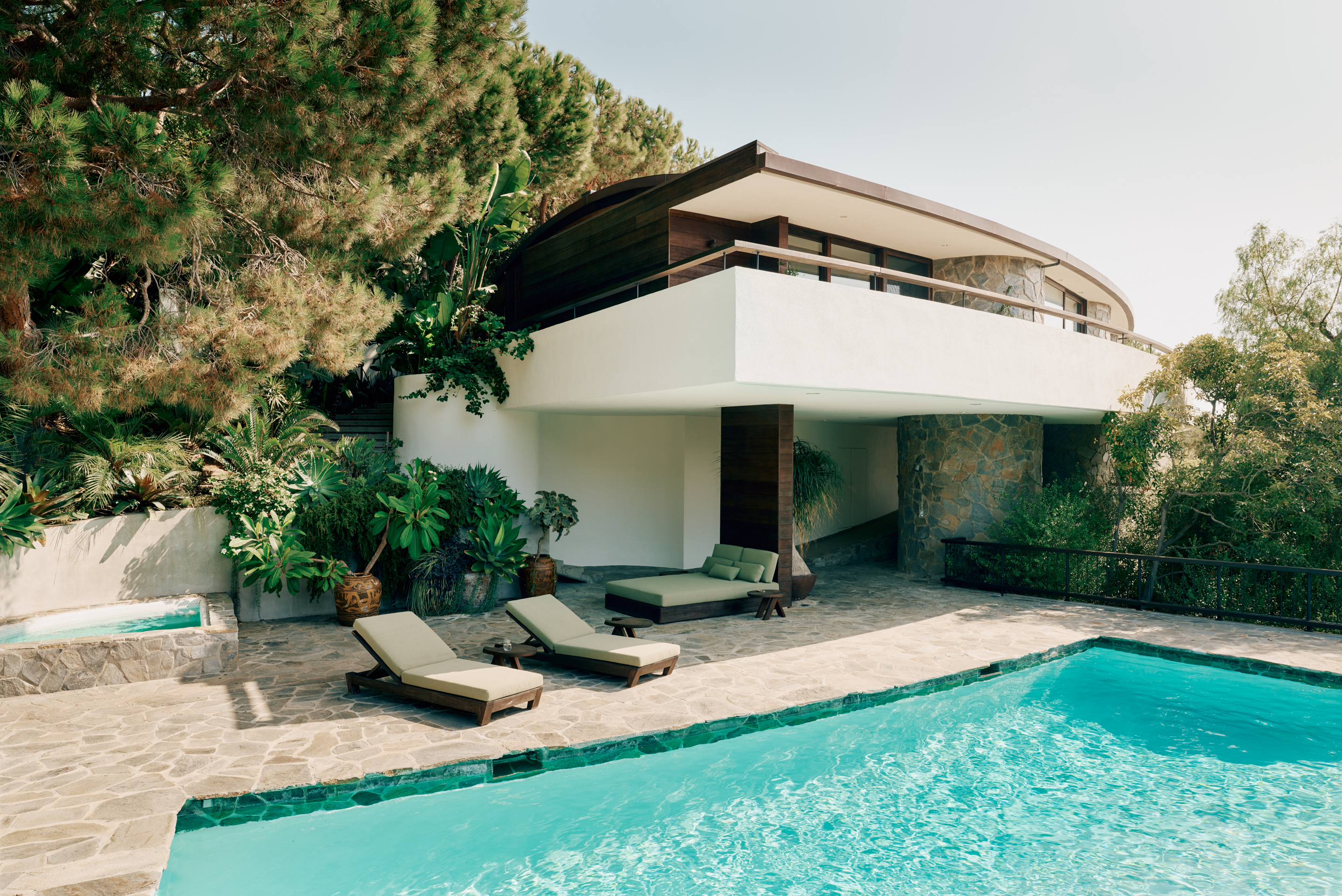view of Lautner's Castle, a midcentury modernist house refreshed for the present day, showcasing arched timber, and stone and wood surfaces among greenery