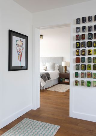 view from hall with artwork on walls to bedroom with grey headboard and door open