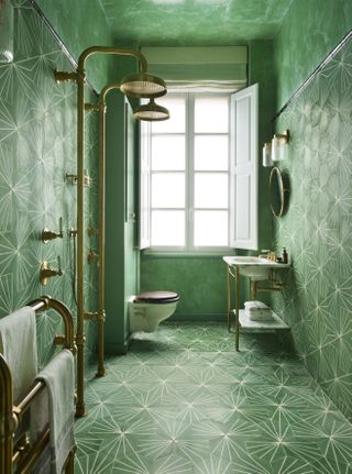 A green bathroom with a green patterned floor and matching wall tiles, brass taps and fixtures and fittings