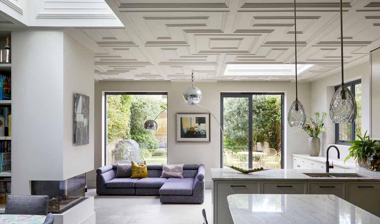 an open plan kitchen space with hanging pendant lights a seating area and decorative ceiling paneling