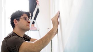 Main in glasses with dark hair rubbing down wall ready for painting