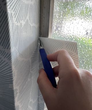 Dori Turner demonstrating how to trim peel and stick wallpaper around window frame