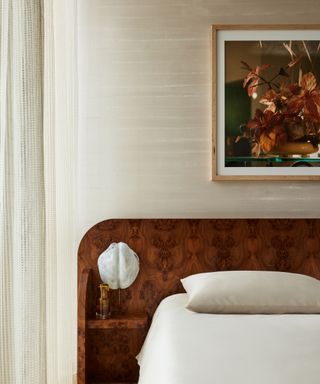 A neutral bedroom with large wooden headboard with a large art piece hanging above