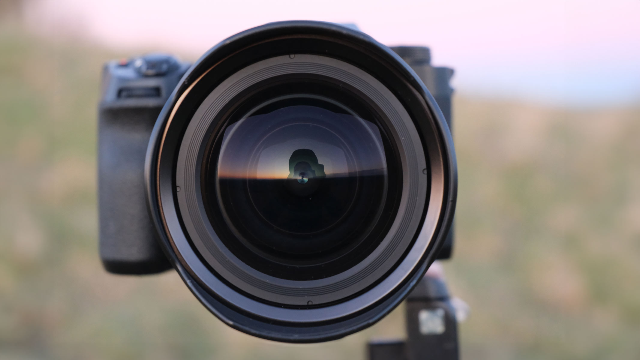 A head-on shot of the Fujifilm XF 8-16mm f/2.8 LM WR lens attached to the Fujifilm X-H2, with a field in the background