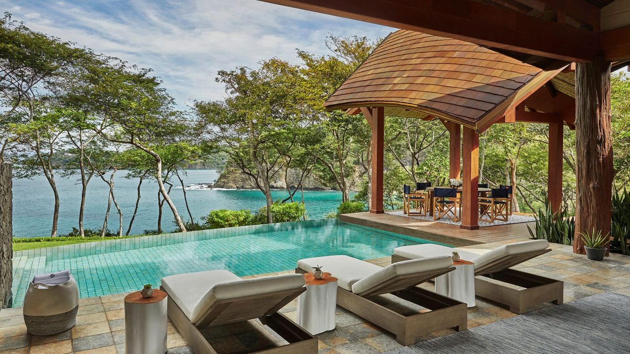 Image of a pool with three lounge chairs over looking the ocean