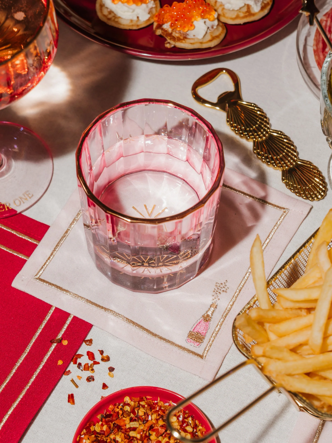 A pair of embroidered cocktail napkins with pink champagne bottles from Vondels