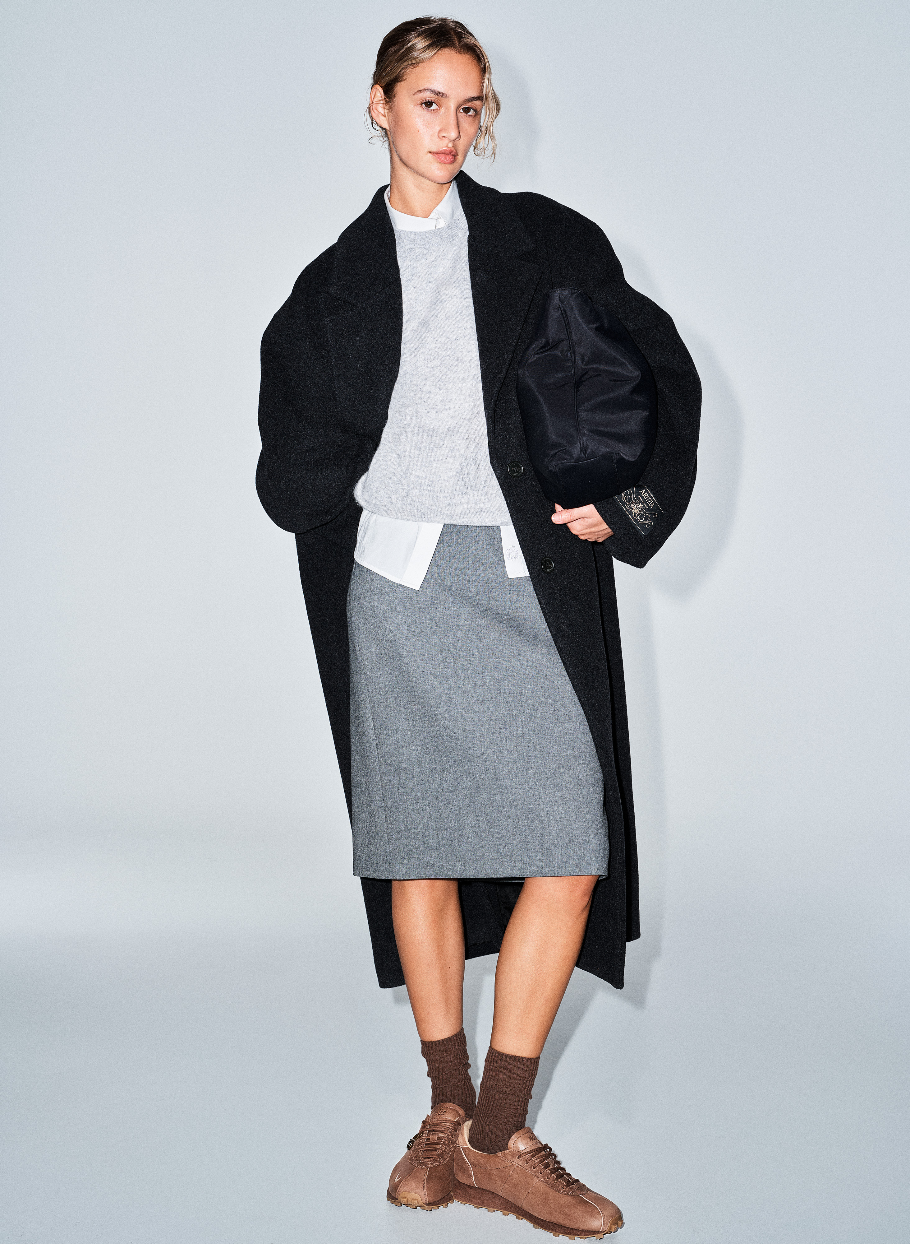 a model wears the aritzia x nike sneakers with a long coat and pencil skirt