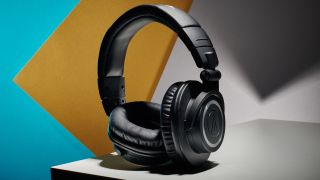 A pair of Audio-Technica ATH-M50xBT2 headphones posed on a white, yellow, and blue background