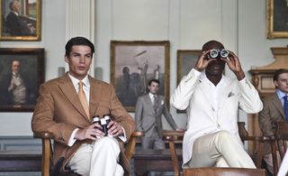 Two models sitting on chairs in suits with binoculars