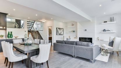 a minimalist style living room with open plan kitchen diner. The couch and dining table is gray and chairs are off white with white walls