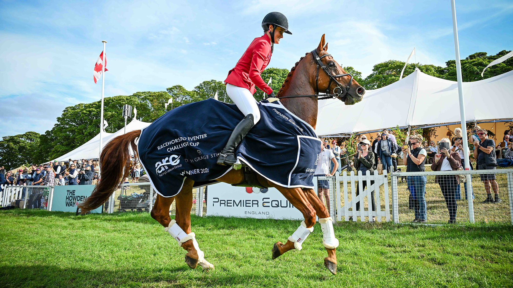 A chestnut event horse who was formerly a racehorse on his lap of honour wearing a navy blue winner&rsquo;s rug with his female rider Bubby Upton in a red jacket with a black safety hat