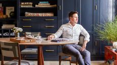 Bryan Graybill sitting at a wooden table in his home with dark blue cabinetry in the background