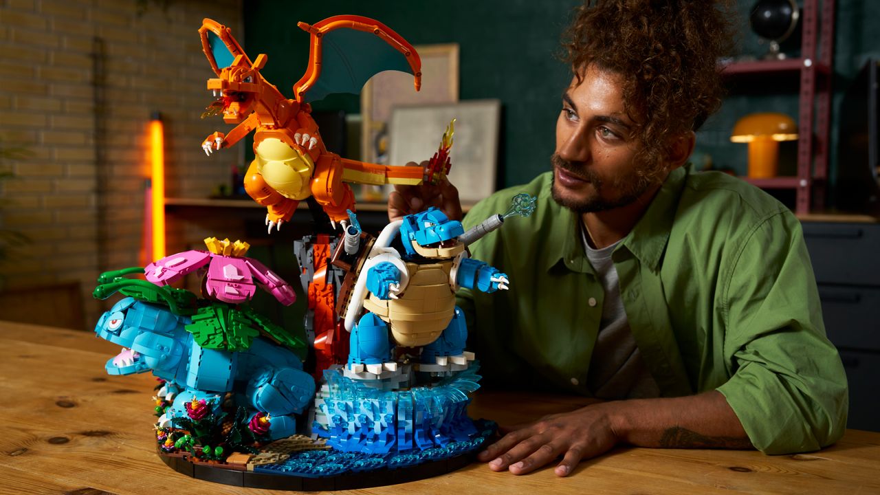 A man looks on at the Lego Venusaur, Charizard, and Blastoise set, sat on a wooden table