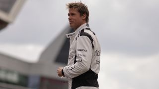 Brad Pitt smiles slightly while standing in his race suit in F1.