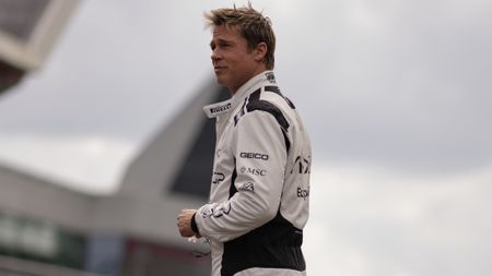 Brad Pitt smiles slightly while standing in his race suit in F1.