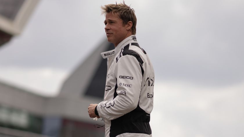 Brad Pitt smiles slightly while standing in his race suit in F1.