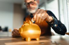 Man puts a coin into a gold piggy bank.