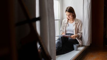 Woman reading book in corner by the window
