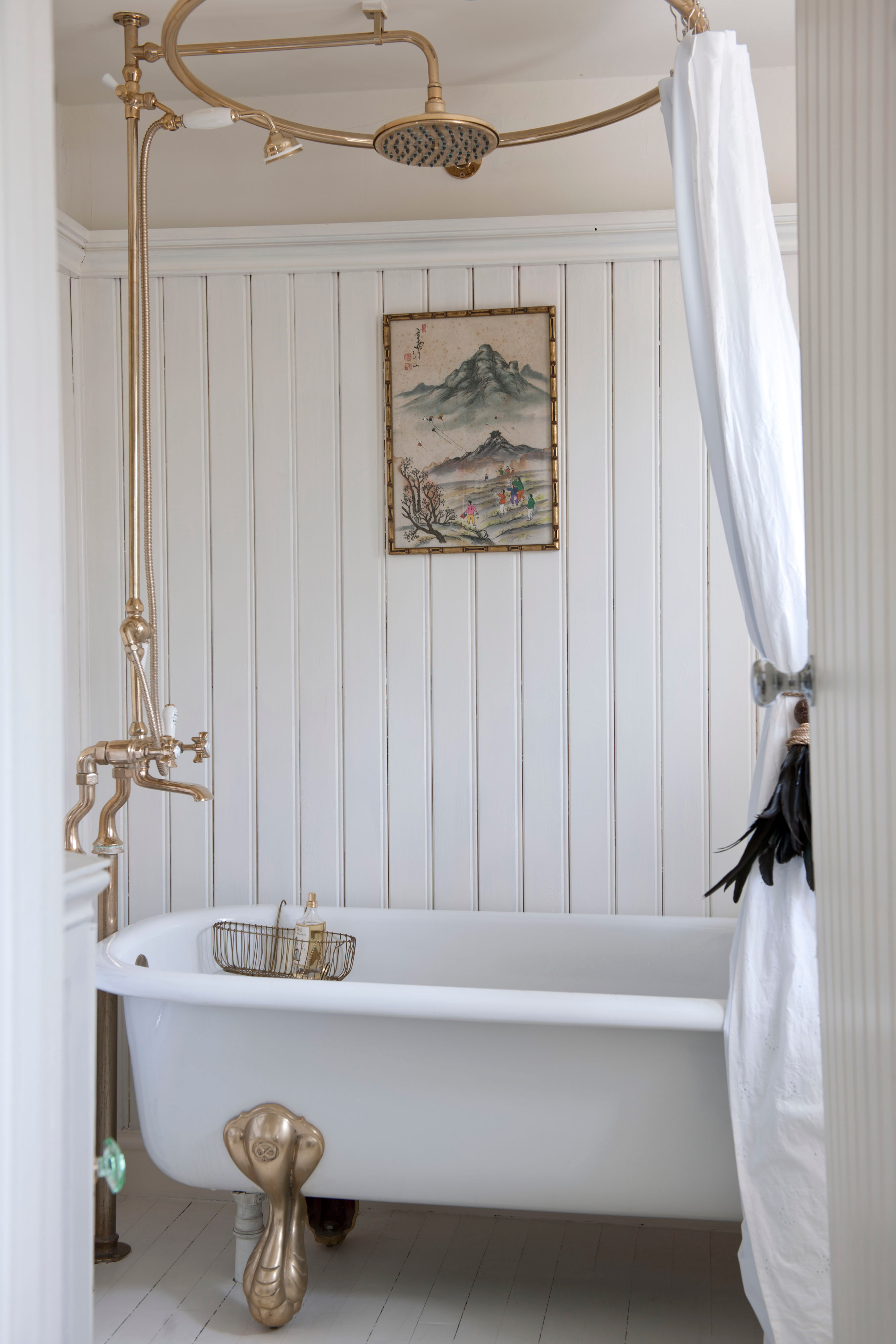 White bathroom with panelled walls and freestanding bath with gold shower rail