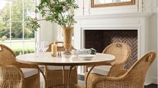 Light-filled dining room area with a herringbone brick fireplace styled with a metal-and-stone circular dining table, woven dining chairs, and brass tabletop accents