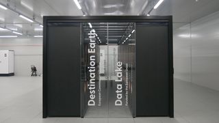 A photo of a computing cabinet within the LUMI supercomputer in Kajaani, Finland. The black cabinet bears the words "Destination Earth, European Commission Initiative, Data Lake, Funded by the European Union" and is situated within a clinical white room.