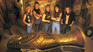 The members of Iron Maiden standing over a sarcophagus