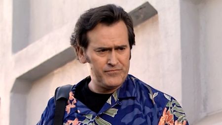 Bruce Campbell, in a blue Hawaiian shirt and slicked back wavy hair, backpack on shoulder, stars in My Name Is Bruce (2007).