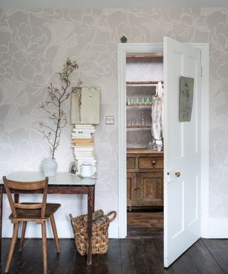 How to wallpaper a room, with pale beige patterned paper in a white room with wooden floorboards and a small desk beside an open door.