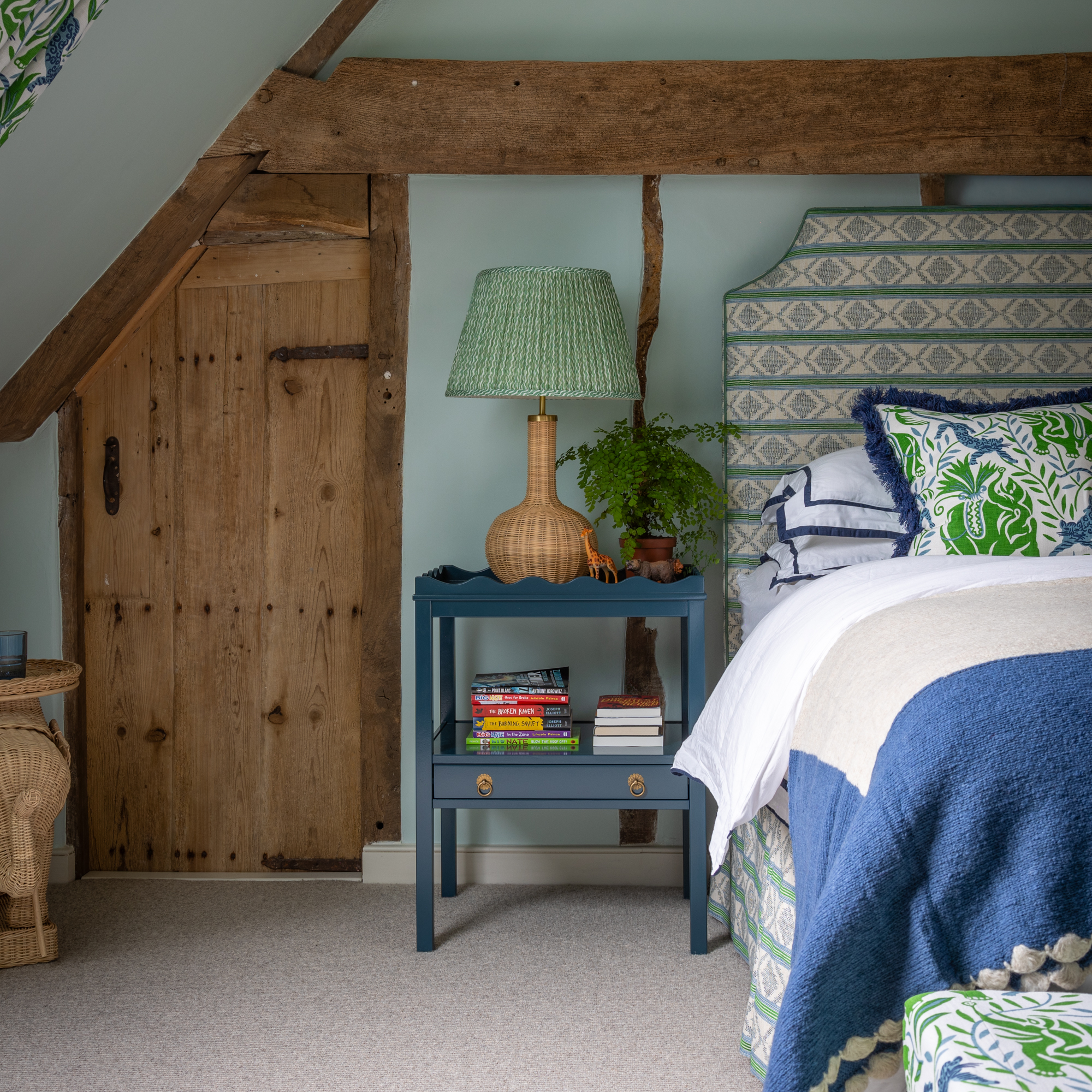 bedroom with blue walls and blue patterned upholstered bed and wicker lamp on blue side table