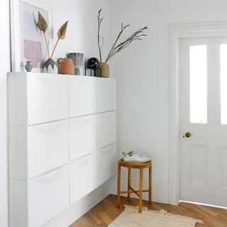 White hallway with grid of wall-mounted shoe storage cabinets, with accessories displayed on top