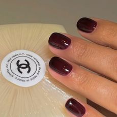 Dark short red nails holding a chanel bar of soap