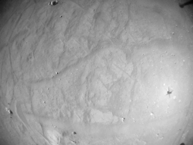 a shadow of a small helicopter is visible on the rocky ground of Mars