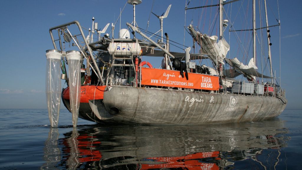 a research vessel floating in the ocean with instruments used to collect seawater seen hanging off the back of the boat
