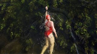 Woman doing front crawl swimming stroke in outdoor water, wearing costume, swim hat and goggles