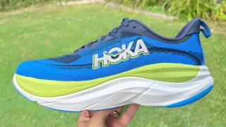 Person holding the Hoka Skyflow running shoe in front of a grassy field