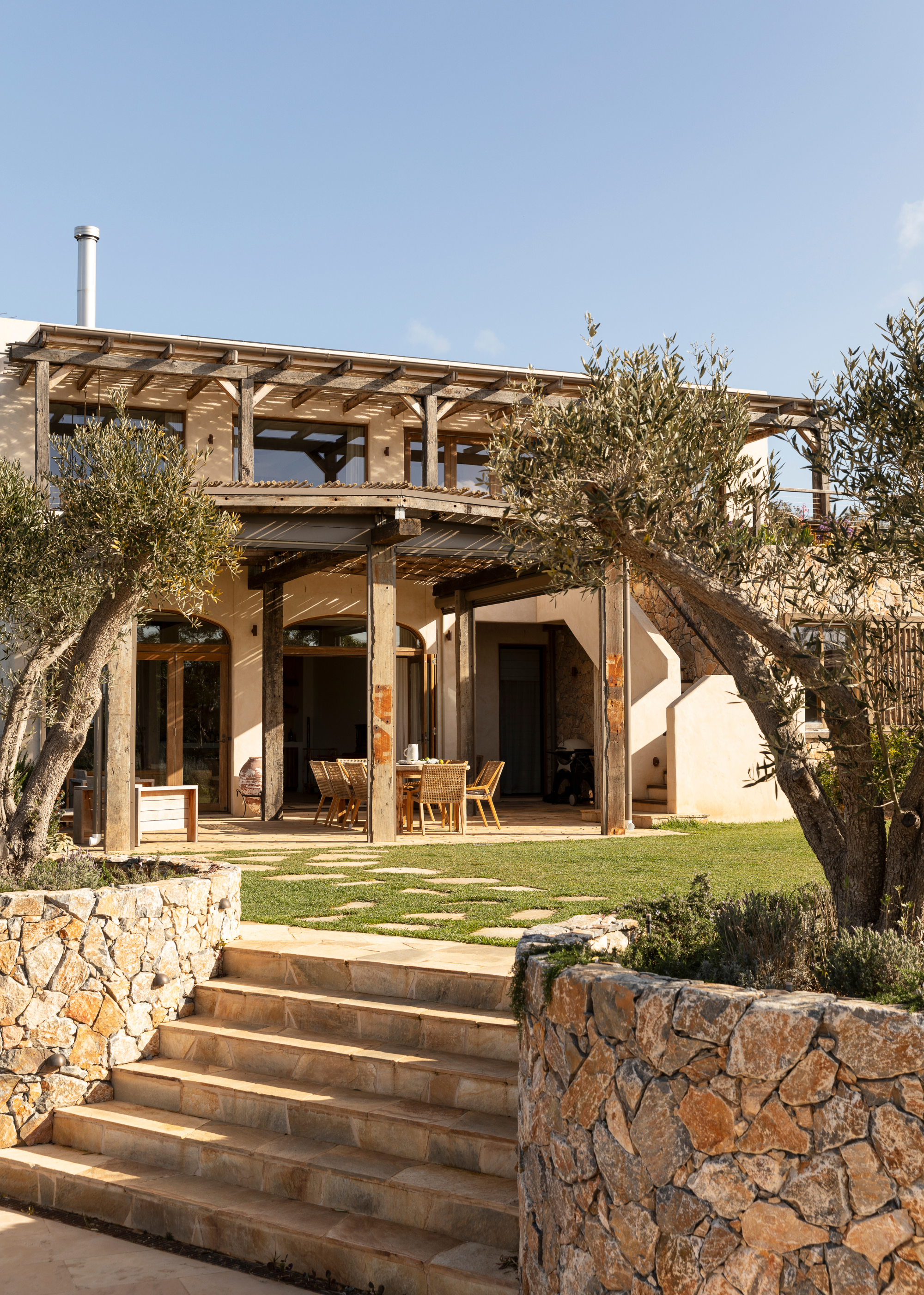 An outdoor garden with olive trees, stone steps, and an outdoor dining room