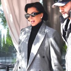 Kris Jenner wears a gray blazer and a burgundy handbag