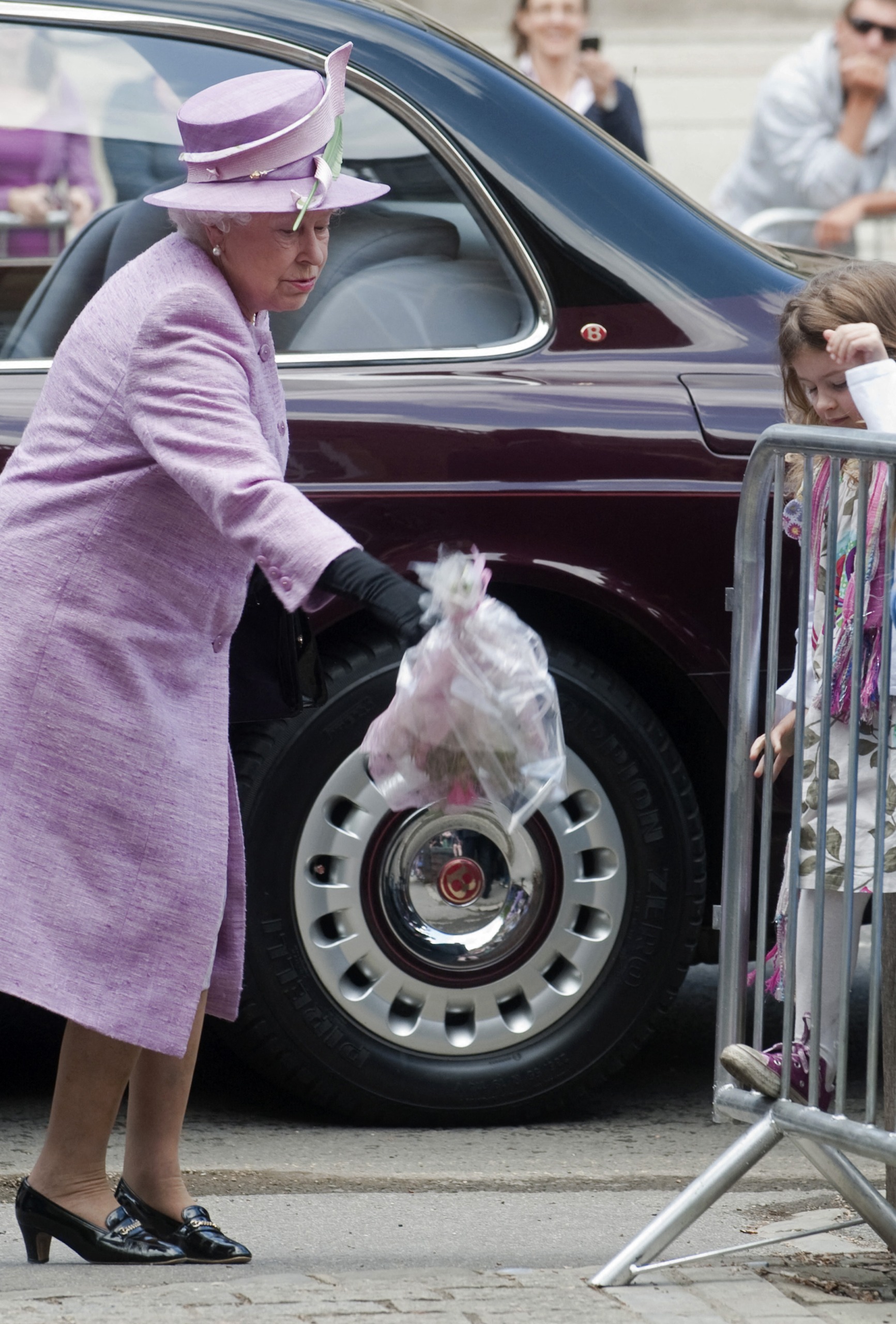 Queen Elizabeth wears a lilac coat and matching hat with a green feather and drops a bouquet given to her by a royal fan in 2010 at Eton