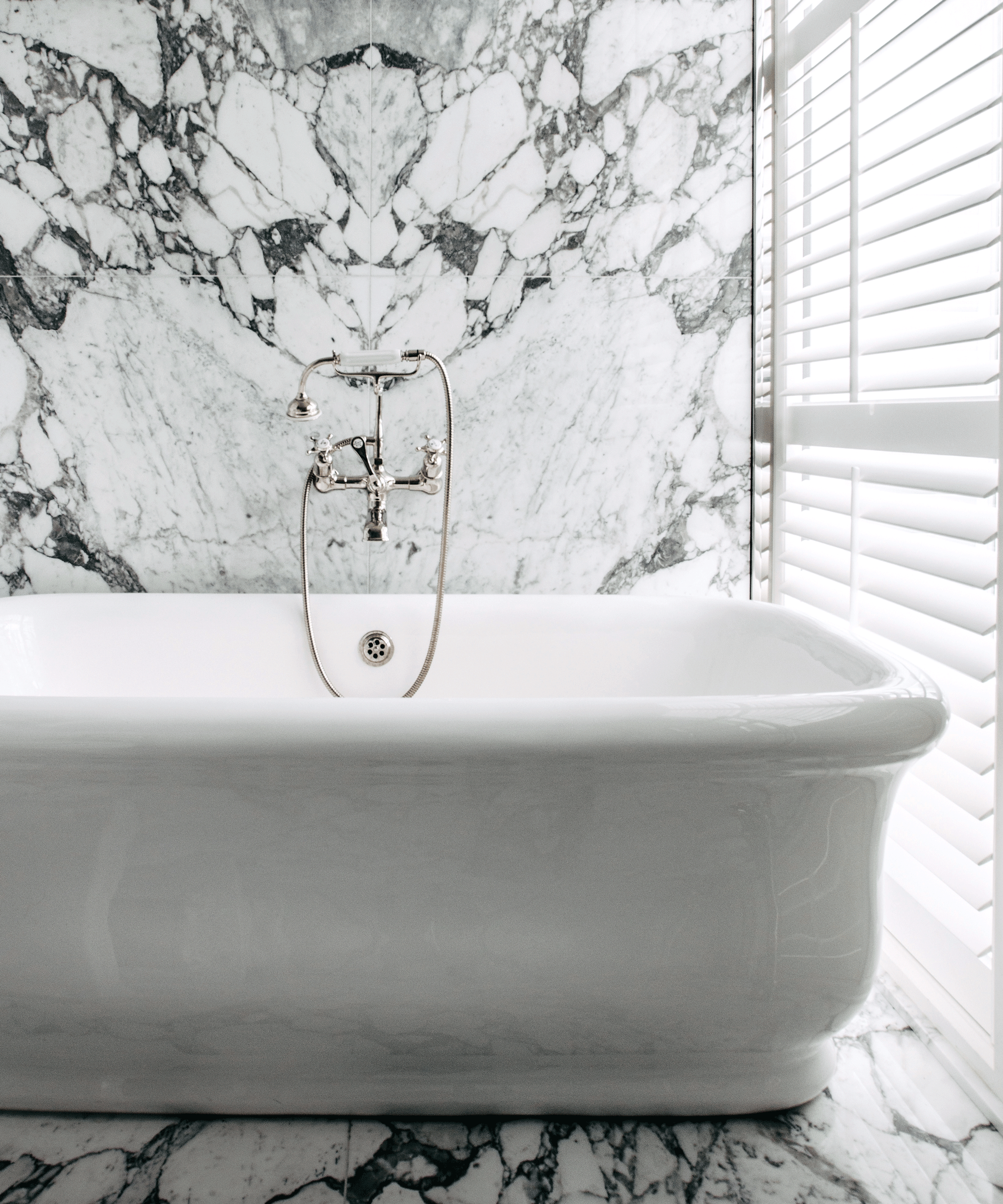 Freestanding white bath against a marble splashback