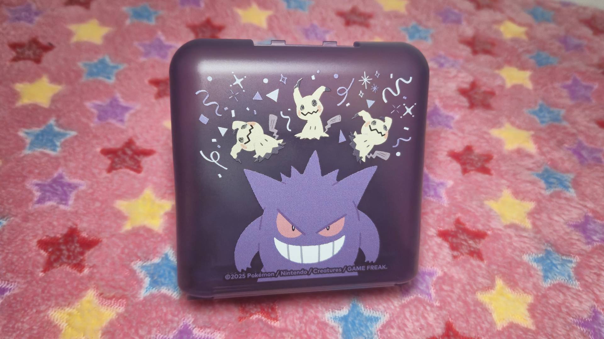 Image of the Hori Gengar and Mimikyu card case sitting on a pink star-patterned blanket.