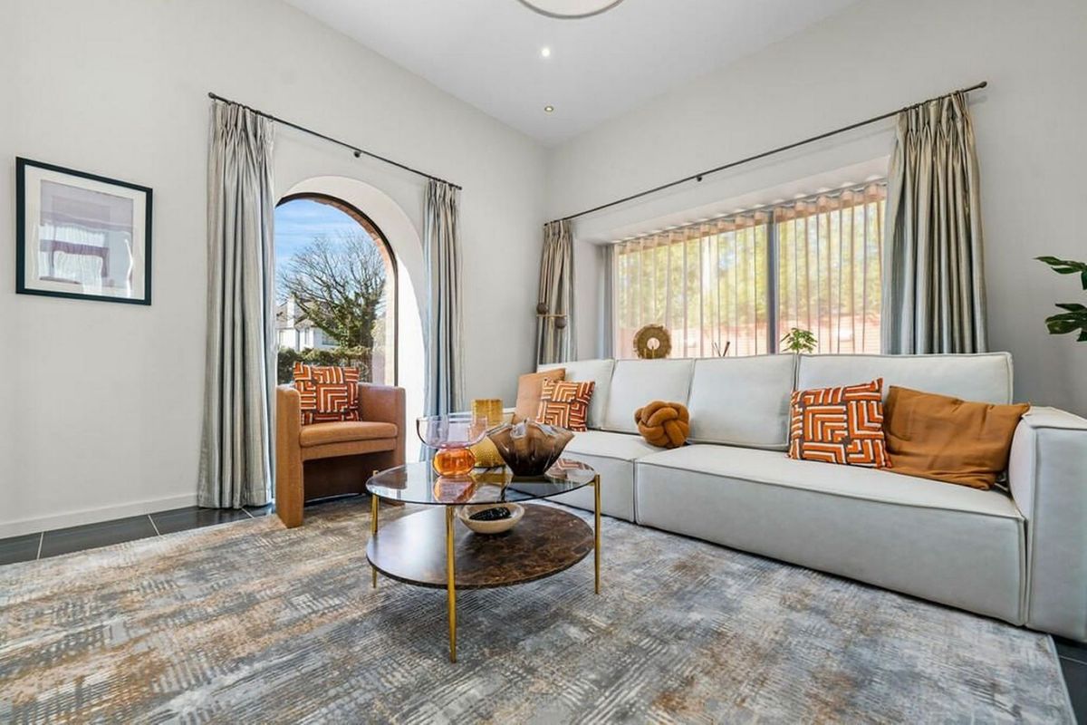 The living room shows a white sofa next to single chair and tall plant which is lit by the many windows