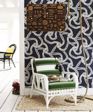 A hallway wallpaper idea with navy blue wallpaper with white knot and rope pattern, and white chair with green cushion