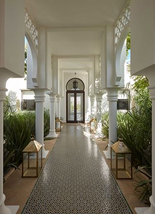 Tiled walkway of the Banyan Tree Tamouda Bay hotel with gold lanterns, leading to double doorway
