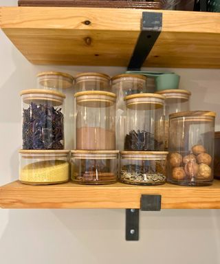 Stacked clear jars on open kitchen shelving filled with herbs spices and condiments such as dried limes