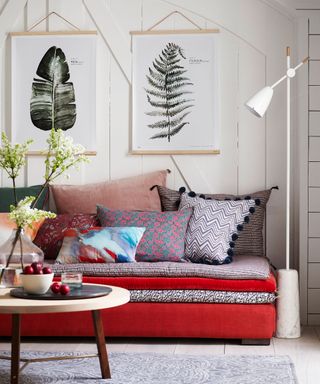 An example of guest bedroom ideas showing a red sofa bed with cushions in front of a white wall with hanging artwork