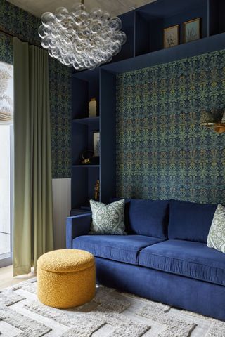 living room with yellow ottoman, blue couch, and blue and green patterned wallpaper