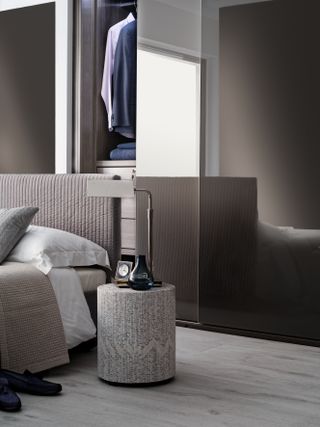 bedroom with closet behind the bed, gray and beige color scheme, upholstered bed, side table, lamp