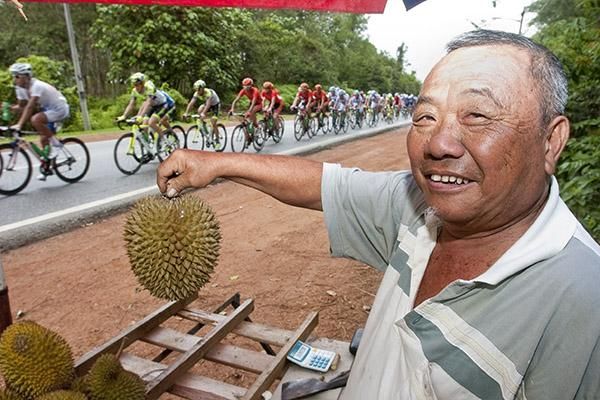 A durian (Malaysian fruit) vendor at his stall as the peloton speeds by.