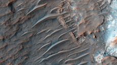 view of mars from orbit showing reddish-brown sand dunes rippling across a rocky surface